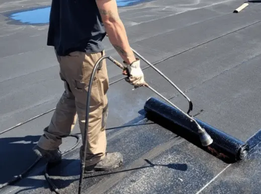 Roofer applying torch-down roofing membrane during a flat roof installation in San Diego